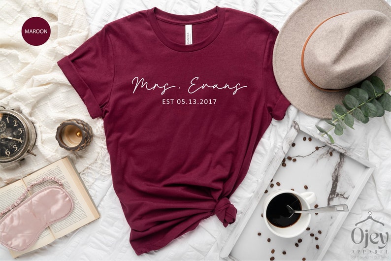 May include: Maroon t-shirt with white text that reads "Mrs. Evans EST 05.13.2017".