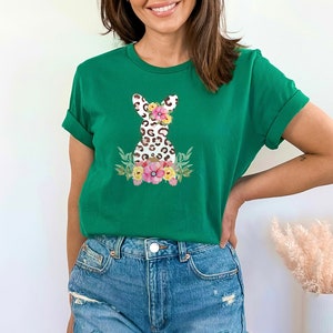 May include: A green t-shirt with a floral design featuring a leopard print bunny. The bunny has a flower crown and is surrounded by pink, white, and yellow flowers.