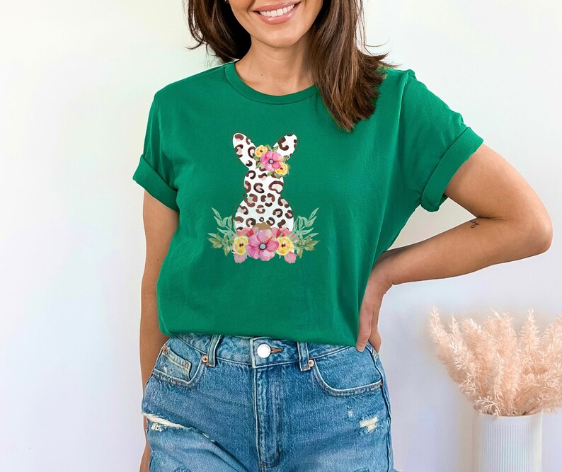 May include: A green t-shirt with a floral design featuring a leopard print bunny. The bunny has a flower crown and is surrounded by pink, white, and yellow flowers.