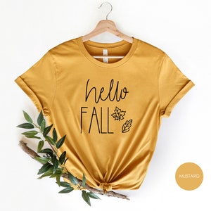May include: A mustard yellow t-shirt with the text "hello fall" and a small leaf design.
