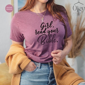 Pode incluir: Uma camiseta marrom heather com o texto "Girl, read your Bible." impresso em preto.