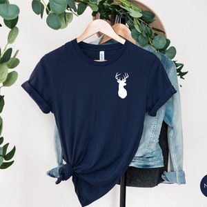 May include: A navy blue t-shirt with a white silhouette of a deer head with antlers on the front. The shirt is folded and hanging on a wooden hanger.