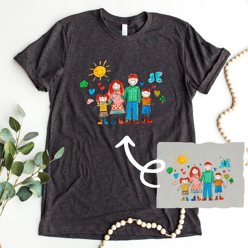Peut inclure: Un t-shirt gris fonc&eacute; avec une illustration color&eacute;e dessin&eacute;e &agrave; la main d'une famille avec un soleil, des c&oelig;urs, des papillons et des tr&egrave;fles. L'illustration repr&eacute;sente une famille de cinq personnes avec deux enfants, un b&eacute;b&eacute;, une m&egrave;re et un p&egrave;re.