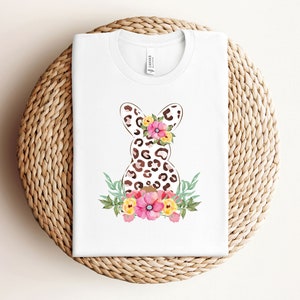 May include: White t-shirt with a brown and black leopard print Easter bunny with pink and yellow flowers.