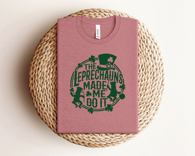 May include: A pink t-shirt with a green graphic that says "The Leprechauns Made Me Do It". The graphic features a leprechaun with a hat and a pot of gold.