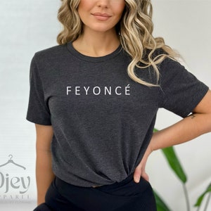 Pu&ograve; includere: Una maglietta grigia scura con il testo "FEYONC&Eacute;" stampato in bianco sul davanti.