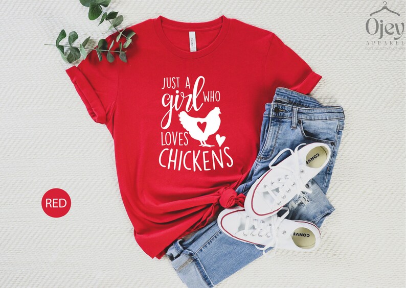 Puede incluir: Camiseta roja con texto blanco que dice "Just a girl who loves chickens" y una silueta blanca de una gallina con un coraz&oacute;n en el pecho.