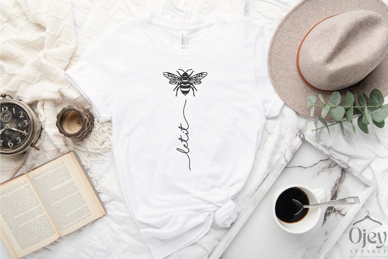 May include: White t-shirt with a black bee graphic and the text "let it" written vertically below the bee.