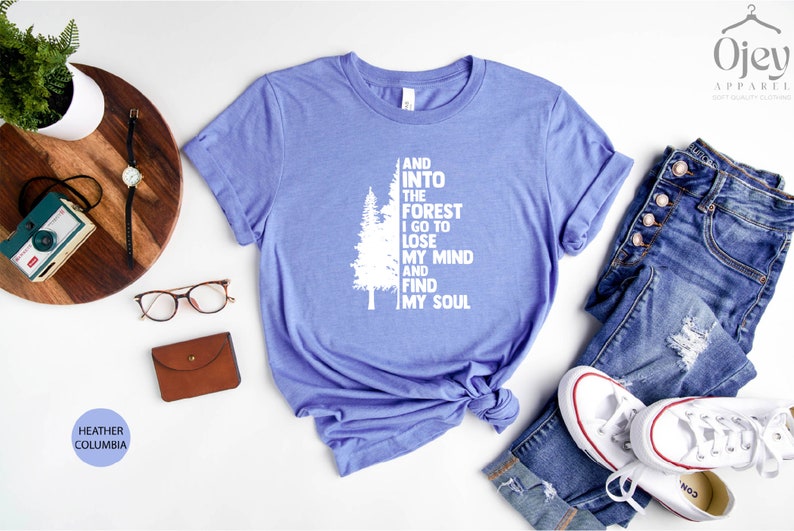May include: A light blue t-shirt with a white graphic of a tree and the text "And into the forest I go to lose my mind and find my soul".