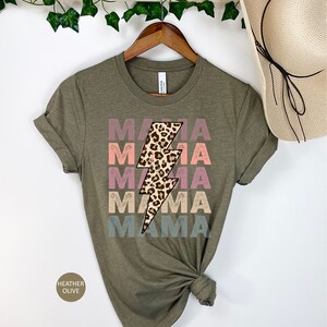Op de afbeelding: Een groen T-shirt met het woord "MAMA" vier keer herhaald in een vervaagd regenboogkleurenschema. Een luipaardprint bliksemgrafiek is gecentreerd op het shirt.
