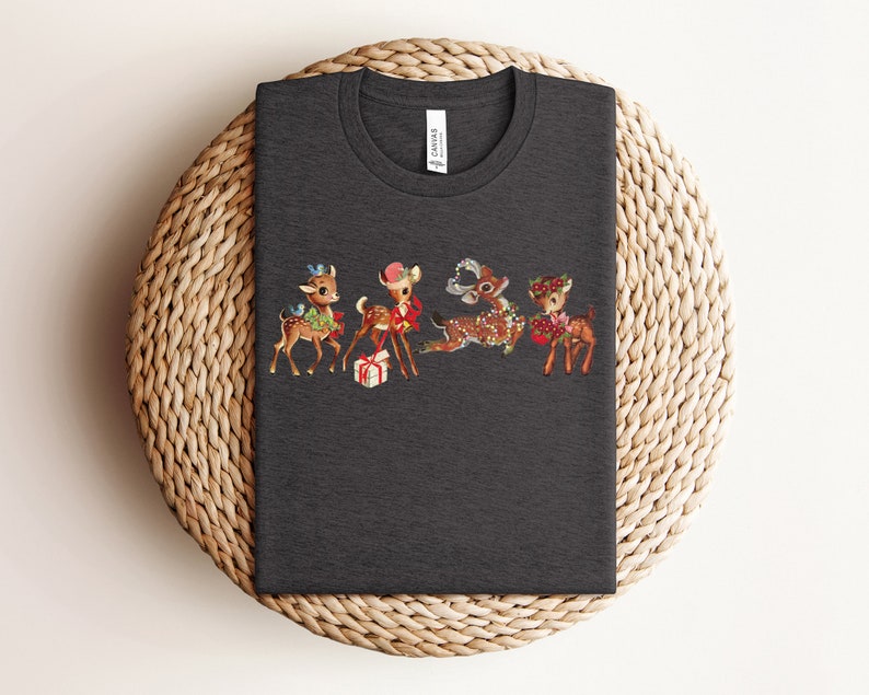 Pu&ograve; includere: Una maglietta grigia scura con un design natalizio vintage con quattro renne dei cartoni animati con accenti rossi e verdi. Le renne indossano cappelli e portano regali.