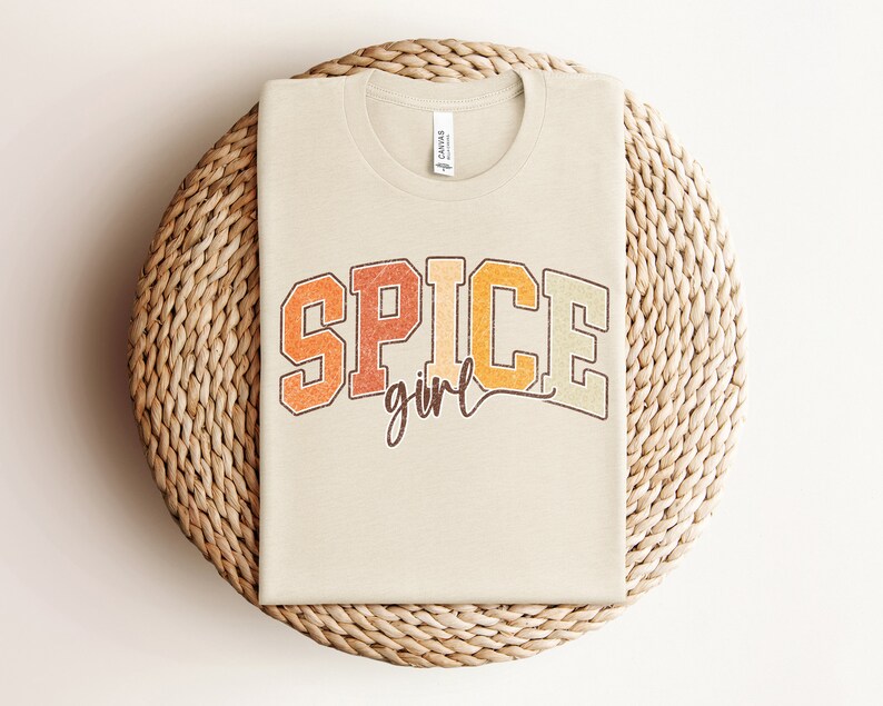 May include: A beige t-shirt with the text "SPICE girl" in a retro-style font with orange, yellow, and brown colors.