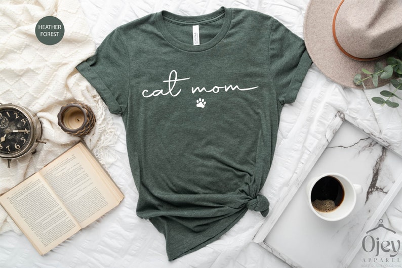 May include: A green heather forest t-shirt with the text "cat mom" in white script with a white paw print below the text.