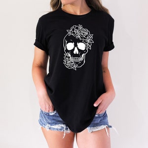 Peut inclure: Un t-shirt noir avec un contour blanc d'un cr&acirc;ne surmont&eacute; de fleurs. Le cr&acirc;ne sourit.
