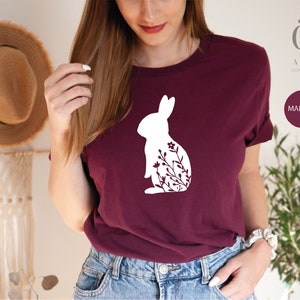 May include: A maroon t-shirt with a white silhouette of a rabbit with flowers. The text "Ojev Apparel" and "Soft Quality Clothing" is printed on the top right corner of the image. The word "MAROON" is printed in a white box on the bottom right corner of the image.