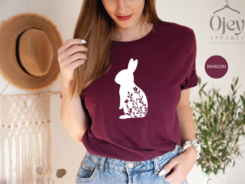 May include: A maroon t-shirt with a white silhouette of a rabbit with flowers. The text "Ojev Apparel" and "Soft Quality Clothing" is printed on the top right corner of the image. The word "MAROON" is printed in a white box on the bottom right corner of the image.