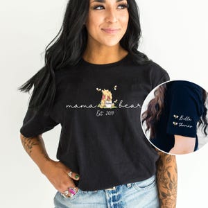 May include: Black t-shirt featuring a Winnie the Pooh illustration and the text "mama bear Est 2019". The t-shirt has a bee design on the sleeve.