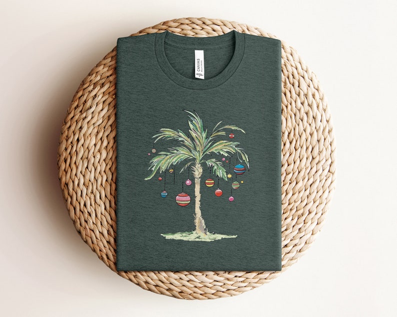 K&ouml;nnte beinhalten: Ein dunkelgr&uuml;nes T-Shirt mit einer Palme, die mit bunten Ornamenten geschm&uuml;ckt ist. Die Palme ist ein Weihnachtsbaum-Design.