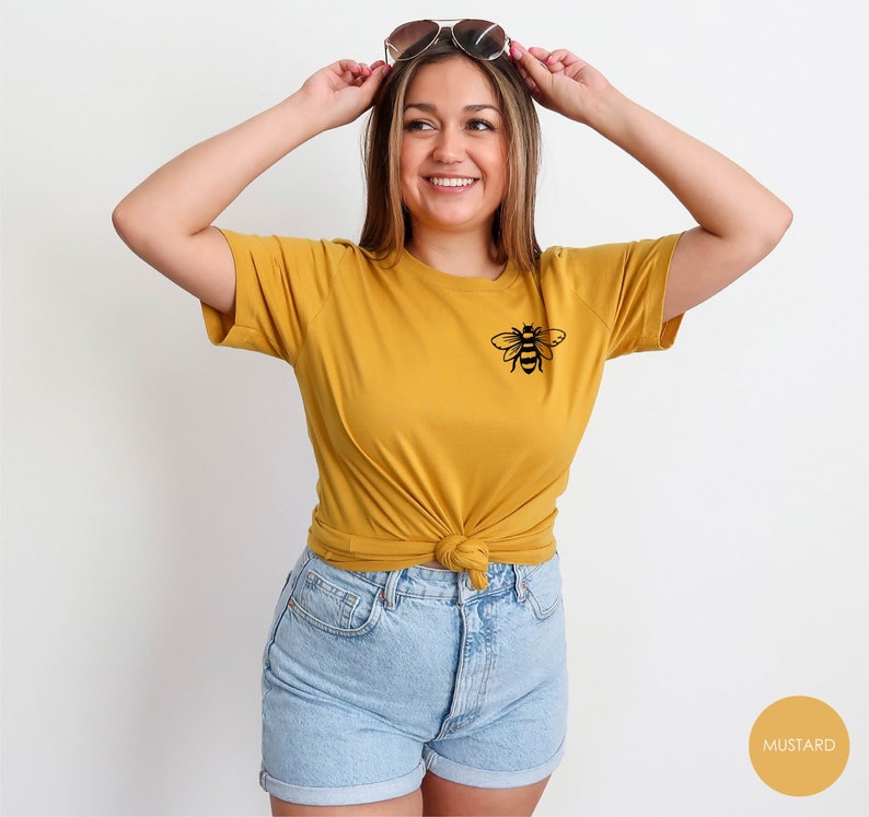 May include: A mustard yellow t-shirt with a black bee graphic on the left chest. The shirt is made of a soft, comfortable fabric and has a relaxed fit.