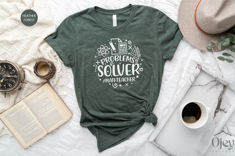 May include: A green t-shirt with a white graphic that says "Problems Solver #MathTeacher". The graphic includes a calculator, pencil, protractor, and atom symbol.