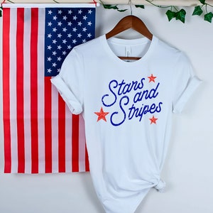 May include: White t-shirt with a blue and red graphic that says "Stars and Stripes".