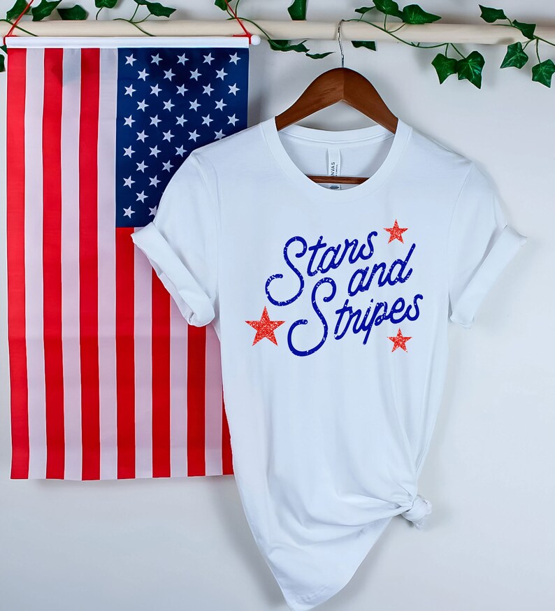May include: White t-shirt with a blue and red graphic that says "Stars and Stripes".