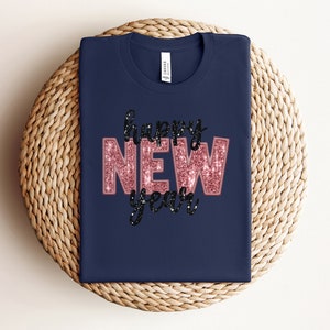 May include: A navy blue t-shirt with the text "happy NEW year" in pink glitter letters with black outlines.