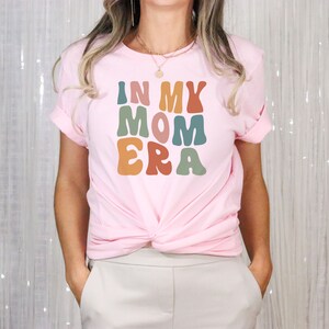 May include: A pink t-shirt with the text "In My Mom Era" in colorful, retro-style lettering.