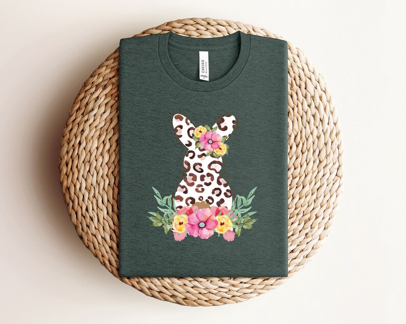May include: A dark green t-shirt with a white and brown leopard print bunny rabbit wearing a floral crown. The bunny is surrounded by pink, yellow, and green flowers.