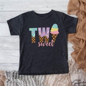 May include: A dark grey t-shirt with a graphic of two ice cream cones that spell out "TWO sweet".