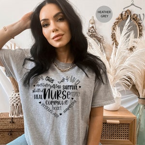 May include: Heather grey t-shirt with a black graphic design that reads "Strong Care Tough Kind Nurture Selfless Support Skilled Heal Nurse Respect Committed Heart Encourage Compassion".