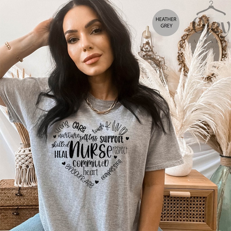 May include: Heather grey t-shirt with a black graphic design that reads "Strong Care Tough Kind Nurture Selfless Support Skilled Heal Nurse Respect Committed Heart Encourage Compassion".