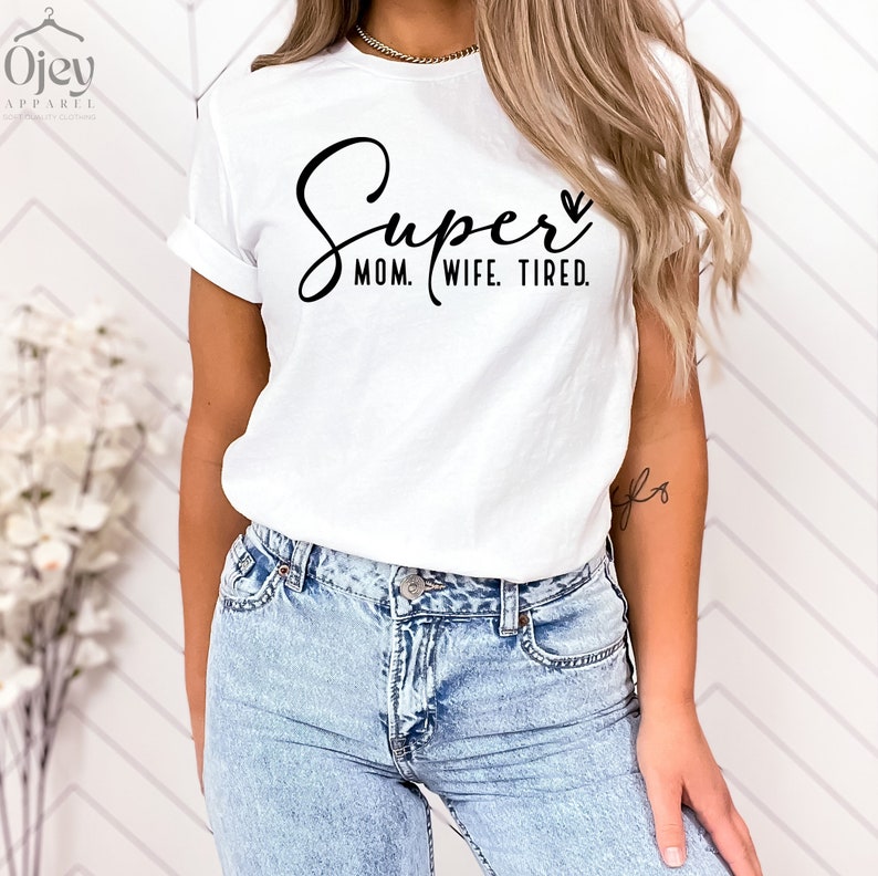 May include: White t-shirt with black text that reads "Super Mom. Wife. Tired." with a small heart symbol.