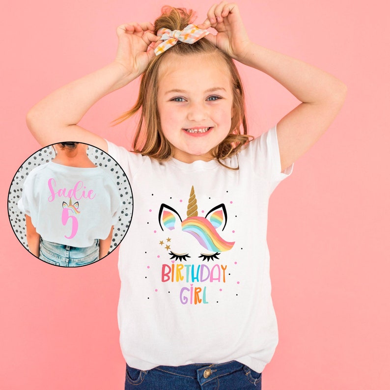 May include: White t-shirt with a rainbow unicorn design and the text "Birthday Girl". The back of the shirt has the name "Sadie" and the number "5" in pink.