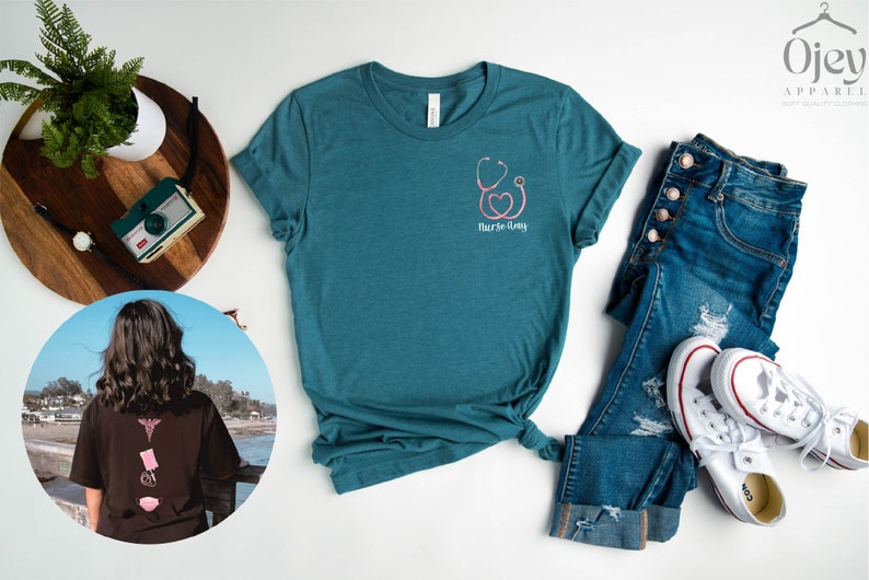 May include: Teal blue t-shirt with a pink stethoscope and heart graphic and the text "Nurse-tastic". The shirt is laid flat on a white surface with a pair of blue jeans and white sneakers.