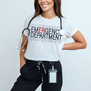 Może przedstawiać: Biała koszulka z nadrukiem "EMERGENCY DEPARTMENT" w kolorze czarnym i czerwonym. Koszulkę nosi osoba ze stetoskopem na szyi i czarnym etui na identyfikator.
