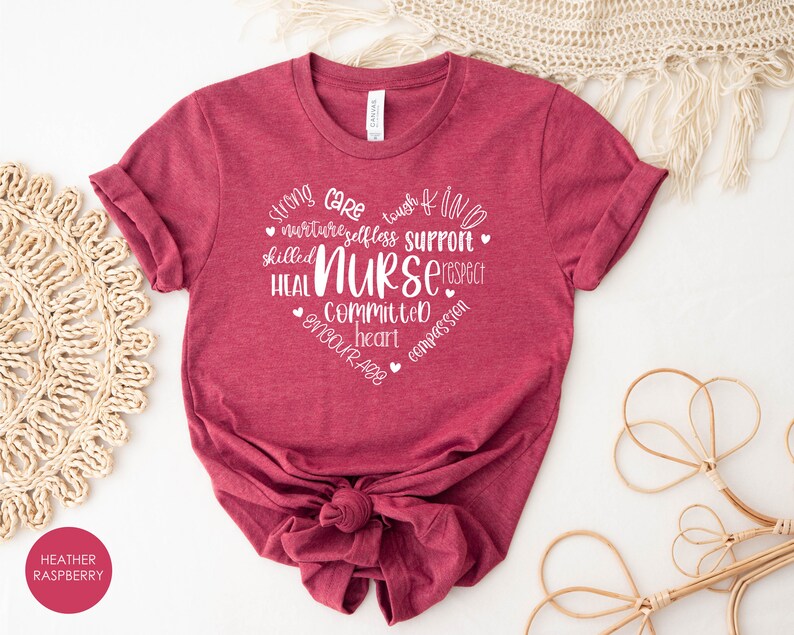 May include: Heather raspberry coloured t-shirt with white text that reads "Strong Care Tough Kind Nurturing Selfless Support Skilled Nurse Respect Heal Committed Heart Encourage Compassion".