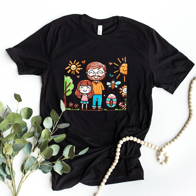 Peut inclure: T-shirt noir avec une illustration color&eacute;e d'un p&egrave;re et de sa fille dans un jardin. L'illustration est dessin&eacute;e dans un style enfantin avec des couleurs vives et des lignes simples.