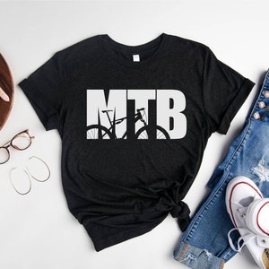 Puede incluir: Una camiseta negra con la palabra "MTB" en texto blanco. La "T" est&aacute; formada por la silueta de una bicicleta de monta&ntilde;a.