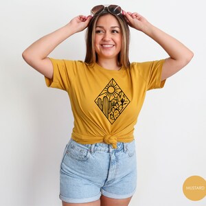 May include: A mustard yellow t-shirt with a black graphic of a desert scene with cacti and a sun. The text "MUSTARD" is visible in the lower right corner of the image.