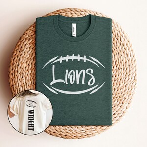 May include: A dark green t-shirt with a white football graphic and the word "Lions" in a white script font. A white t-shirt with the number "15" and the name "Wright" in black text is shown in the background.