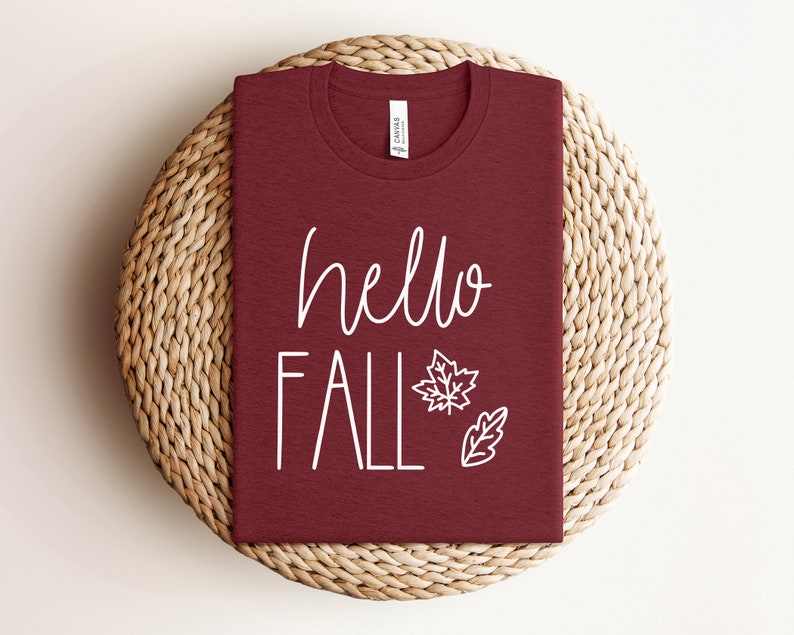 May include: A maroon t-shirt with the text "hello fall" in white lettering and a white outline of a maple leaf and an oak leaf.