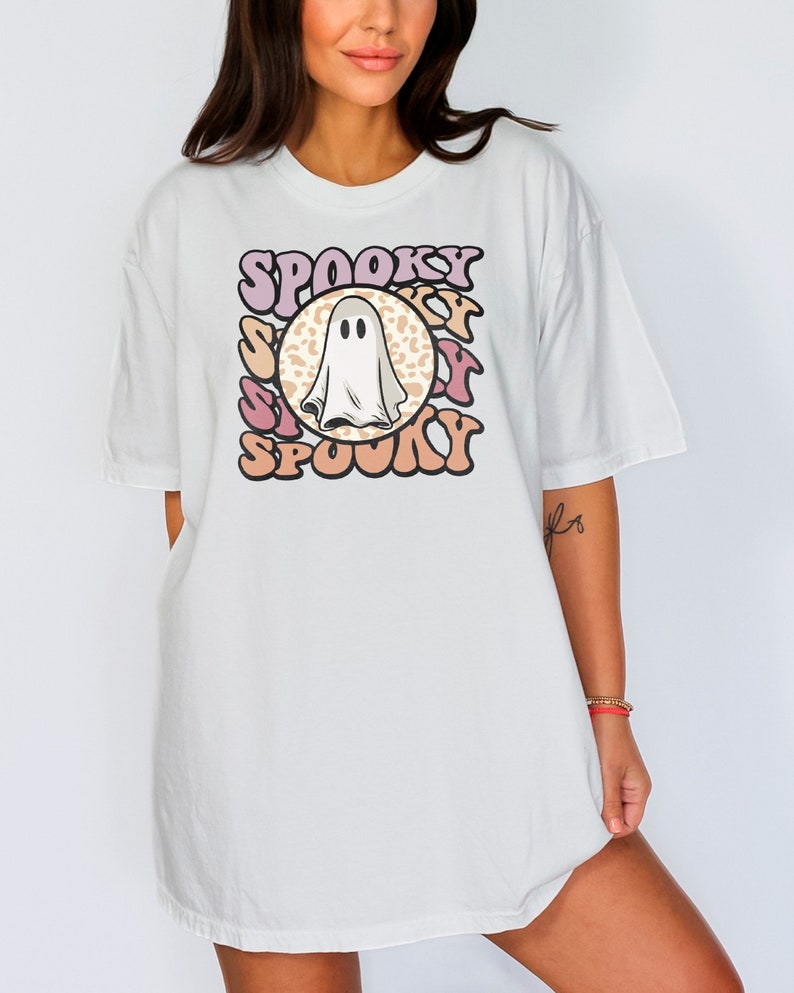Puede incluir: Camiseta blanca de gran tama&ntilde;o con un gr&aacute;fico de un fantasma en un c&iacute;rculo con la palabra "Spooky" escrita en una fuente retro alrededor del c&iacute;rculo.