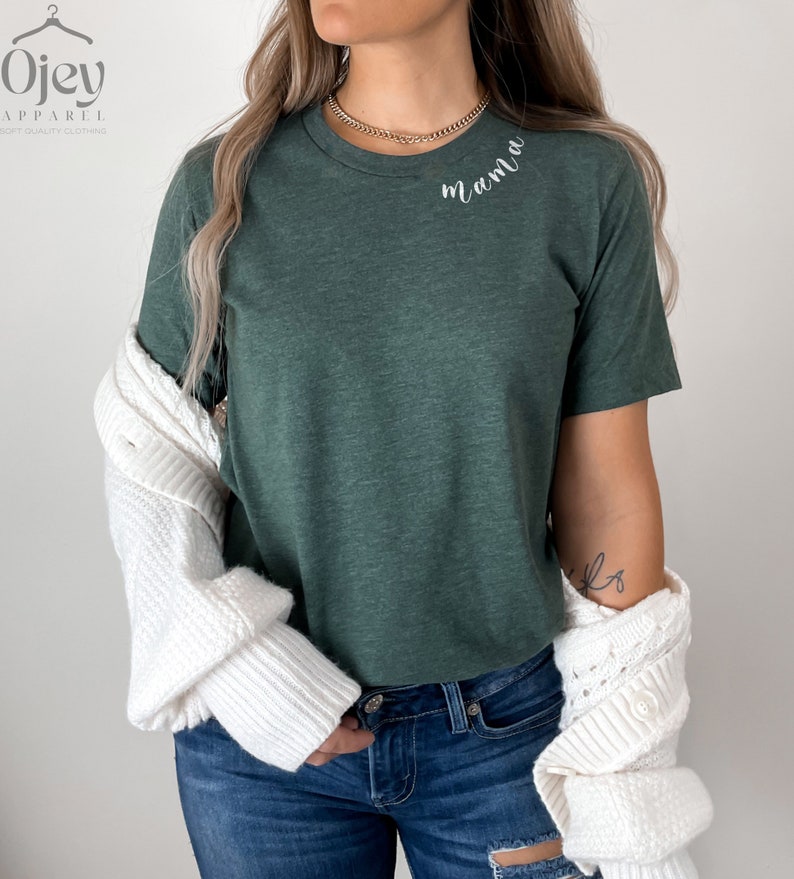 K&ouml;nnte beinhalten: Ein gr&uuml;nes T-Shirt mit dem Wort "mama" in wei&szlig;er Kursivschrift auf der Brust.