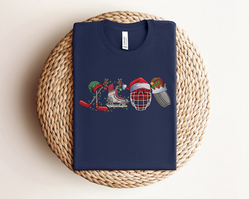 May include: A navy blue t-shirt with a Christmas-themed hockey design. The design features a hockey stick, a hockey skate, a hockey helmet, and a Santa hat.