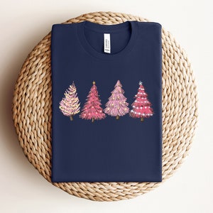 May include: A navy blue t-shirt featuring a design of four pink Christmas trees with gold lights and decorations.