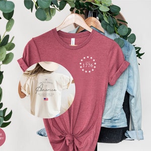 Peut inclure: T-shirt de couleur framboise heather avec un cercle blanc d'&eacute;toiles et le texte "Since 1776" sur le devant. Le dos du t-shirt porte le texte "United States of America The Land of the Free" avec un petit drapeau am&eacute;ricain.