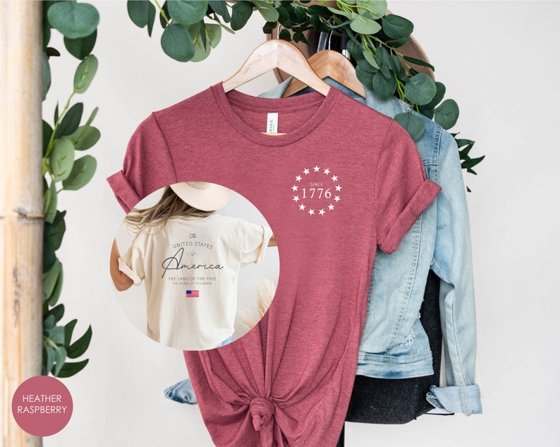 Peut inclure: T-shirt de couleur framboise heather avec un cercle blanc d'&eacute;toiles et le texte "Since 1776" sur le devant. Le dos du t-shirt porte le texte "United States of America The Land of the Free" avec un petit drapeau am&eacute;ricain.