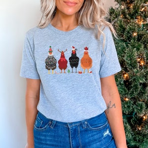 Może przedstawiać: Szary T-shirt z grafiką pięciu kurczak&oacute;w w świątecznych czapkach i swetrach. Kurczaki stoją w rzędzie i mają r&oacute;żne kolory pi&oacute;r i swetr&oacute;w.