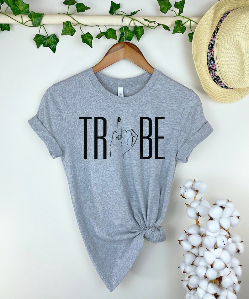 May include: Gray t-shirt with black text that reads "TRIBE" and a black line drawing of a hand giving the middle finger with a ring on the finger.